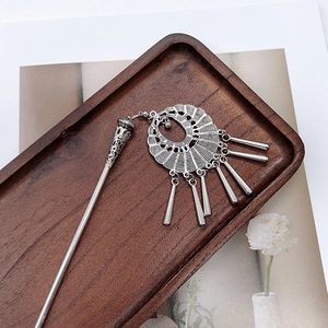 Detail view of a vintage silver hair pin with fringe tassels on a wooden tray