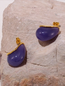 Detailed close-up of dark purple resin stud earrings on a textured stone background