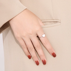 Detail of a minimalist silver heart ring worn on hand with a beige suit background