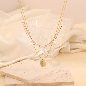 Détail du collier doré à double rangée avec perles colorées et pendentif papillon