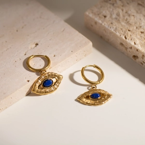 Detail of 18K gold plated evil eye earrings with lapis lazuli on stone background