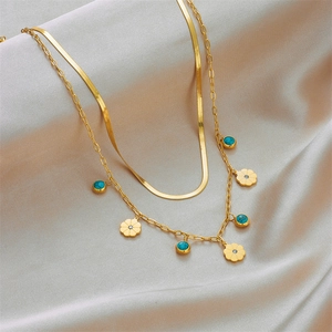 Zweilagige goldene Schlangenkette mit türkisfarbenem Blumenanhänger auf Seidenhintergrund