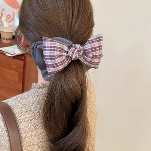 Detail of purple plaid fabric bow hair tie styled on a ponytail in a warm cafe setting