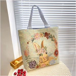 Detail of canvas tote bag featuring embroidered rabbit wreath and striped handles