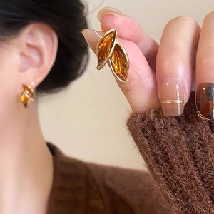 Elegant gold leaf-shaped stud earrings with amber resin detail on female model