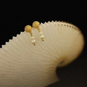 Macro shot of gold shell earrings with dangling pearls on a white spiral shell background