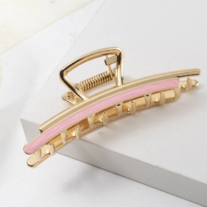 Macro view of gold metal hair claw clip with pink striped accents on a geometric background
