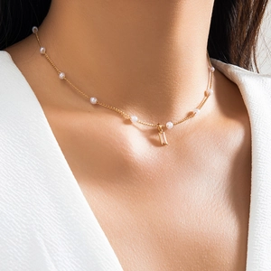Close-up of gold chain necklace featuring white pearls and a rectangular pendant on neck