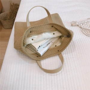 Detailed macro of the woven straw tote bag featuring a smooth zip and metal snap closure