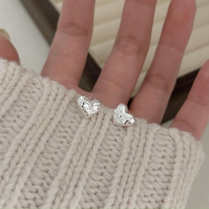 Detailed view of silver heart stud earrings resting on a white knitted sweater sleeve