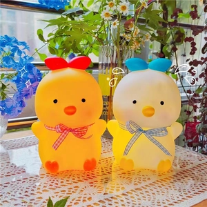 Close-up of cute cartoon chick and duck LED night lights glowing on a lace tablecloth