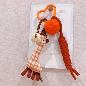 Detail of plush giraffe keychain with orange plaid pattern and red braided rope loop