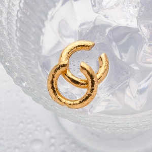 Detail of gold-plated textured metal earrings displayed on clear ice cubes