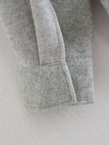 Close-up detail of grey wool blend fabric and stitching on a loose jacket cuff