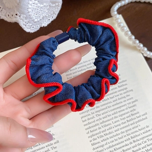 Detailed view of navy blue denim hair scrunchie with contrasting red stitched edges