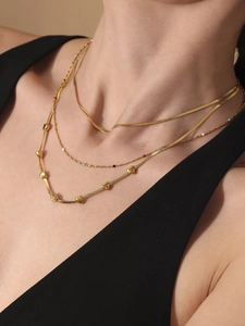 Close-up of layered 18k gold plated necklaces featuring heart charms and snake chain detail
