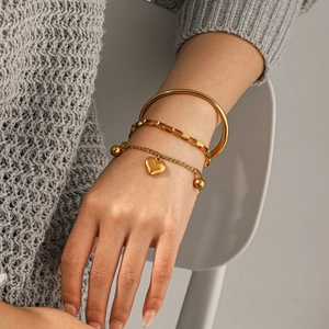 Vista detallada de un conjunto de pulseras de acero de titanio dorado con colgante de corazón.