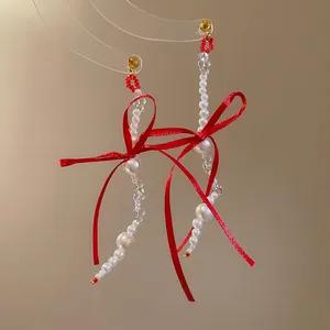 Elegant drop earrings featuring red silk bows and white pearls on a warm minimal background