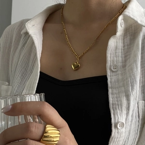 Detail of gold heart pendant necklace and textured ring on model with linen shirt