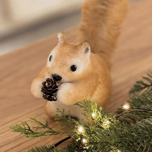 Realistic Christmas squirrel ornament holding a pine cone on festive evergreen branches