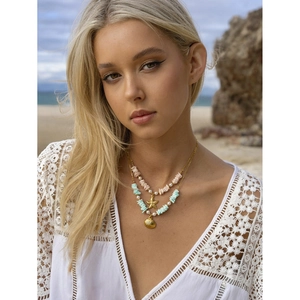 Detail of layered gold necklace with pink turquoise beads and sea shell charms