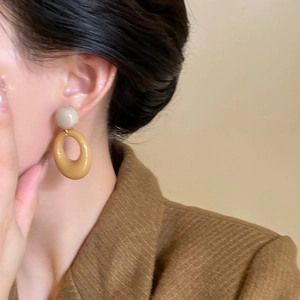Close-up of caramel retro resin oval hoop earrings worn with a brown tweed jacket