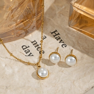 Elegant gold pearl necklace and stud earrings set on a textured beige background