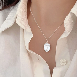 Detail of 925 sterling silver necklace featuring an abstract face pendant on a white shirt