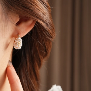 Close-up of golden basket cluster earring with white pearls and sparkling rhinestones