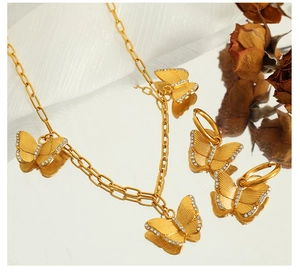 Detailed view of a gold butterfly necklace and earrings set on a mirror background