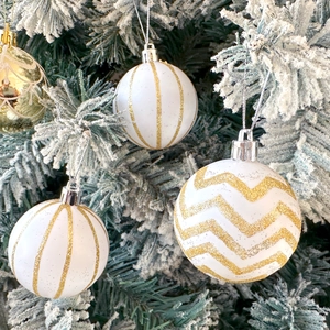 Detail of white Christmas balls with gold glitter patterns hanging on snowy tree branches