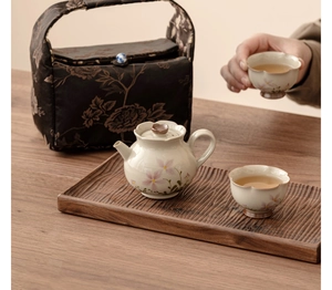 Macro shot of ceramic tea cup with pink daisy pattern being held by hand on wooden tray