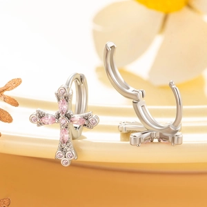 Silver hoop earrings with pink zircon cross charms on a ceramic jewelry tray