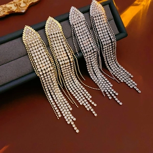 Macro view of gold and silver tassel earrings with glittering crystals on a luxury box