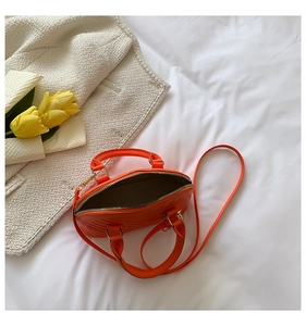 Top view of orange quilted mini shell bag on white fabric with yellow tulips