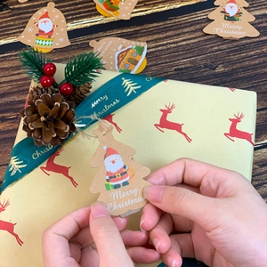 Close-up of Christmas kraft paper gift tag held by hand over festive holiday boxes
