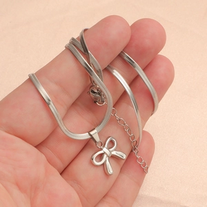 Hand holding silver butterfly bow pendant with flat snake chain in polished titanium steel
