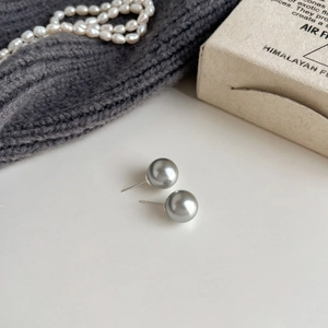 Detailed view of grey pearl stud earrings on a minimalist white surface with soft props