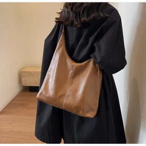 Side view of a large brown soft leather tote bag on a model in a minimalist setting