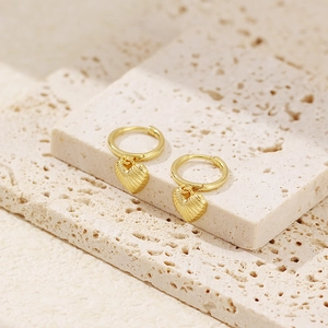 Close-up of gold heart-shaped hoop earrings with shell texture on beige stone