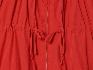 Detail of red windbreaker jacket featuring drawstring waist and metal zipper closure