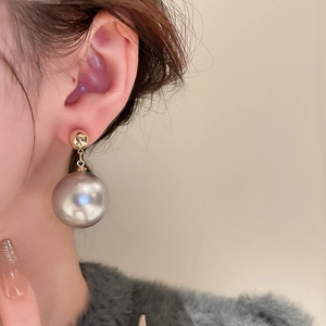 Detailed view of elegant gold metal stud and large grey faux pearl drop earring