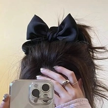 Close-up of a black silk satin hair tie with a large bow worn on hair for styling