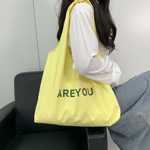 Detailed view of yellow canvas shoulder bag with green AREYOU lettering on a model