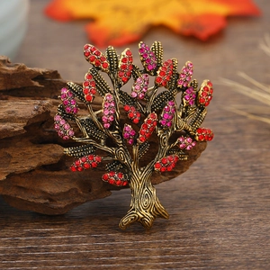 Vintage gold Tree of Life brooch featuring red and pink crystals on rustic wood base