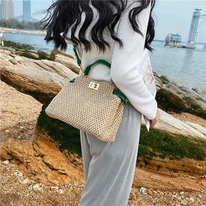 Detail of hand-woven straw bag with green leather handles and gold lock in outdoor setting
