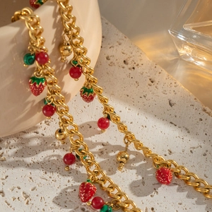 Dettaglio catena placcata oro 18K con ciondoli a fragola rossa su fondo in pietra