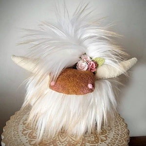 Detail of a white shaggy highland cow plush with a pink flower and beige horns