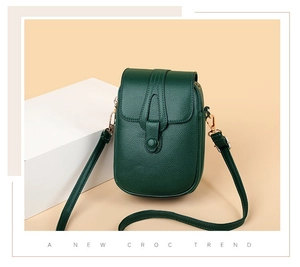 Detail of dark green crossbody phone bag with croc texture and golden hardware