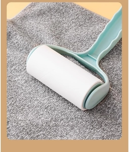 Close-up of lint roller with light blue handle on grey fabric showing easy-tear white sheets